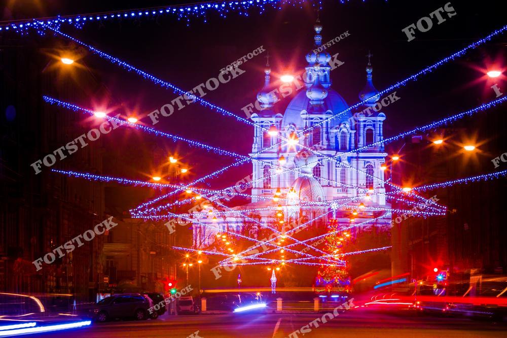 Фотография зимнего Санкт-Петербурга с видом на Смольный собор в праздничной атмосфере Нового года и Рождества. Снежные улицы, заснеженные крыши и зимняя река Нева создают атмосферу северной столицы России в холодное время года. Мягкий зимний свет подчеркивает голубые и белые фасады собора, архитектурные детали и историческую красоту города. Панорамный и центрический ракурс позволяет передать масштаб и величие Смольного собора, гармонично сочетая природные элементы и городскую инфраструктуру. Изображение подходит для туристических публикаций, зимних коллекций фотографий, постеров, сувенирной продукции и интерьерного оформления.